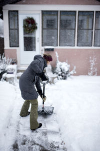 Woman shoveling snow outside house