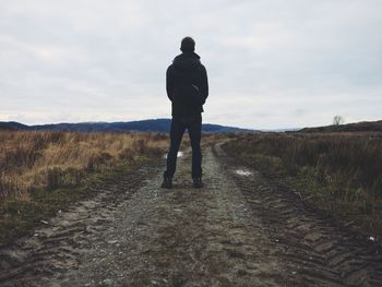 Rear view of man walking on field against sky