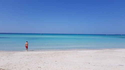 Shirtless man wading in sea against clear sky