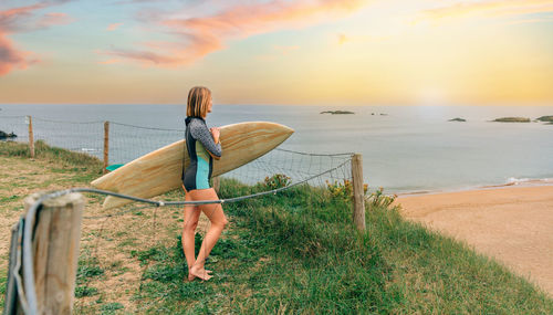 Surfer woman with surfing suit and surfboard looking at the beach