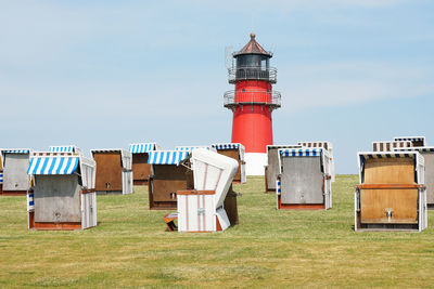 Hooded beach chairs on field and lighthouse against sky