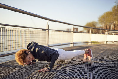 Side view of determined young woman doing push-ups on metallic footpath