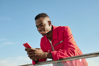 Smiling young man in red jacket looking at smart phone outdoors
