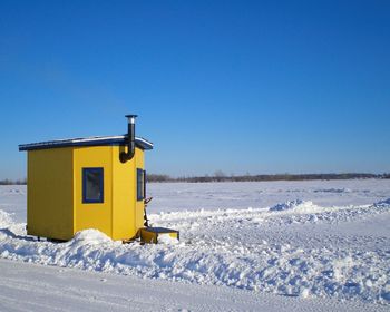 Yellow cabin on snow covered landscape against clear blue sky
