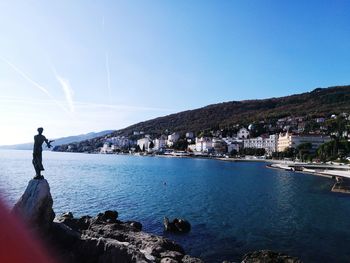 Woman standing on rock by sea against clear blue sky