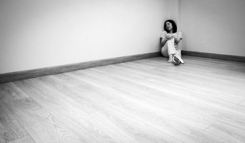 Full length of woman sitting on hardwood floor against wall