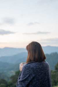 Rear view of woman looking at mountain against sky during sunset