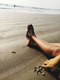 Low section of person relaxing on sand at beach