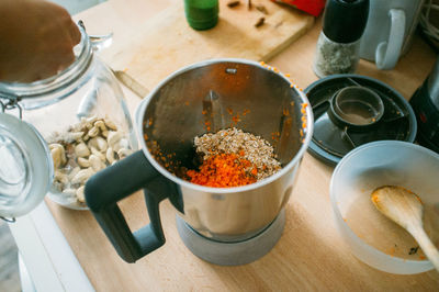 High angle view of cropped hand taking nuts from jar with food in grinder on table