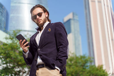 Low angle view of businessman using mobile phone while standing outdoors