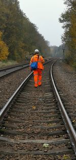 Rear view of male worker walking on railroad track amidst trees