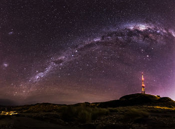 Low angle view of illuminated communications tower against milky way