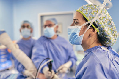 Female doctor wearing protective face mask standing with colleague in operation room at hospital