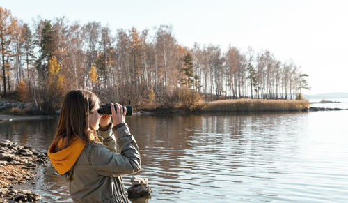 Rear view of woman photographing lake against sky