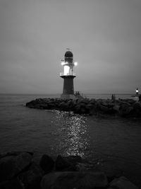 Lighthouse by sea against sky at night