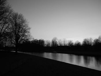 Bare trees by river against clear sky