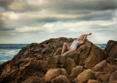 Seductive young woman wearing one piece swimsuit on rocks at beach