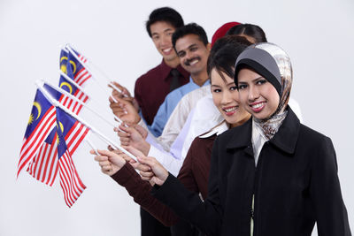 Portrait of smiling colleagues holding malaysia flags against white background