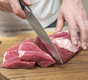 Midsection of man cutting meat on board