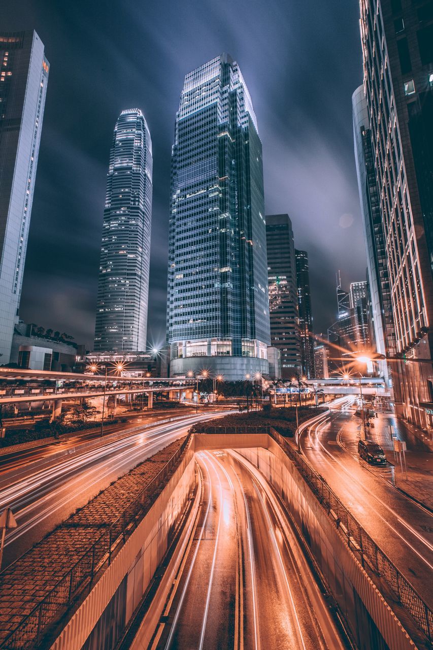 speed, long exposure, light trail, motion, illuminated, night, architecture, building exterior, city, transportation, high street, outdoors, skyscraper, built structure, blurred motion, sky, high angle view, no people, road, urban scene, cityscape, modern