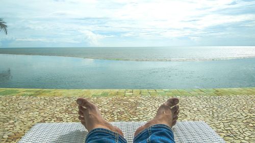 Low section of man standing on sea shore against sky