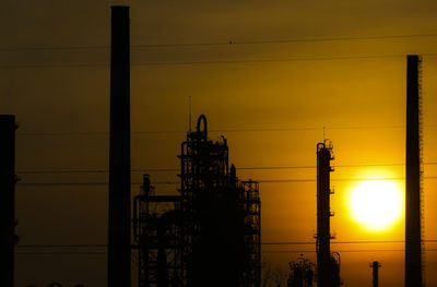 Silhouette of factory against sky during sunset