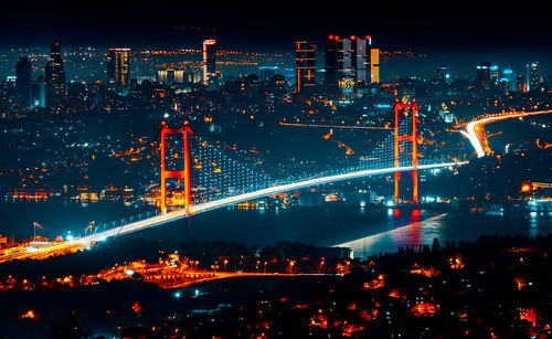 Illuminated city by river against sky at night