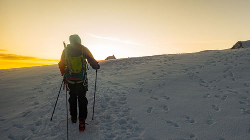 Rear view of hiker hiking on snow covered land during sunset