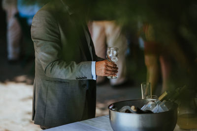 Midsection of man holding wineglass while standing at table indoors