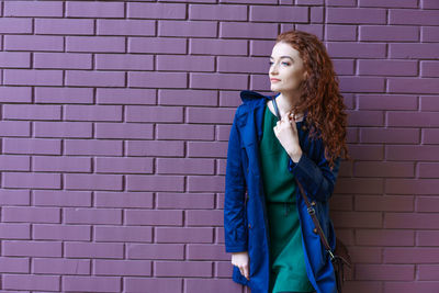 Thoughtful attractive redhead young woman in blue raincoat looking at camera