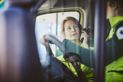 Paramedic talking on phone while looking at coworker in ambulance
