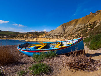 Boat moored on beach against blue sky