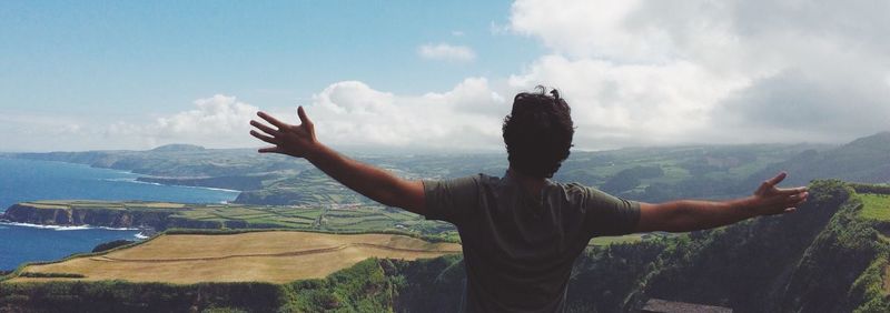 Rear view of man with arms outstretched standing on mountain against sky