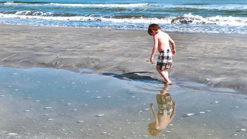 Full length of shirtless man walking on beach