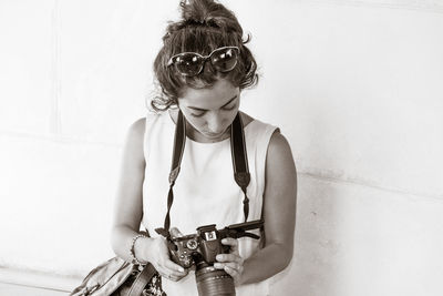 Young woman holding camera while standing by wall