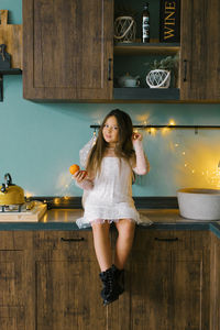 A beautiful girl of seven years old is sitting in the kitchen and holding tangerines in her hands