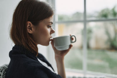 Young woman drinking coffee by window