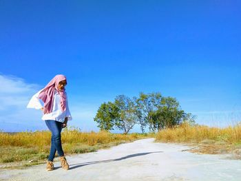 Woman standing on road against clear blue sky