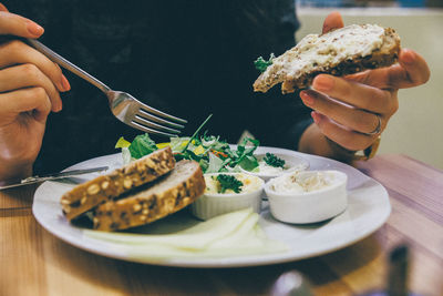 Midsection of woman holding bread over food in plate