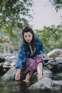 Young woman sitting on rock against trees