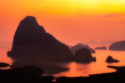 Silhouette rocks in sea against orange sky