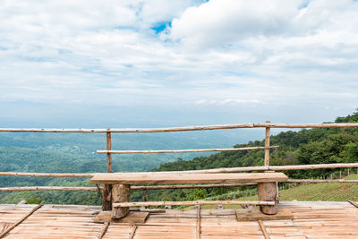 Wooden railing by sea against sky