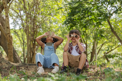 Side view of sibling looking through binoculars against trees