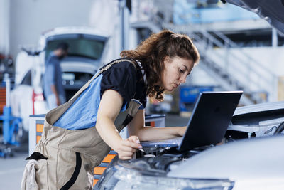 Side view of young woman using laptop while standing in city