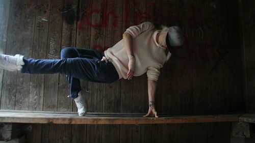 Side view of man dancing against wooden wall