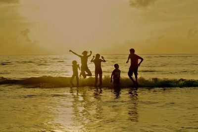 Silhouette people in sea against sky during sunset