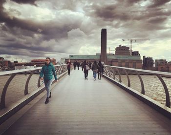 People walking on bridge in city against sky