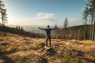 Enthusiastic traveller stands on a stump in a clear-cut forest and looks down into the valley