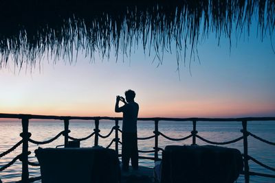Silhouette man photographing by sea against clear sky during sunset