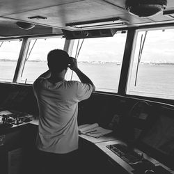 Rear view of man looking through binoculars while standing in ship